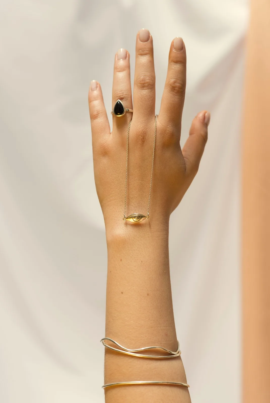 Mano con anillo gota de ónix, collar ojo y pulseras onda